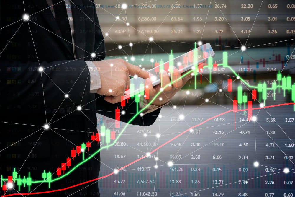 A close-up of a professional using a digital tablet featuring a data-rich interface and overlays of various financial markets charts.